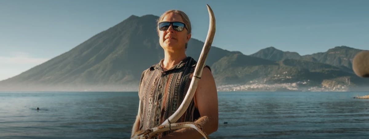 Daniel on dock holding rare antler flute — mountains and lake backdrop